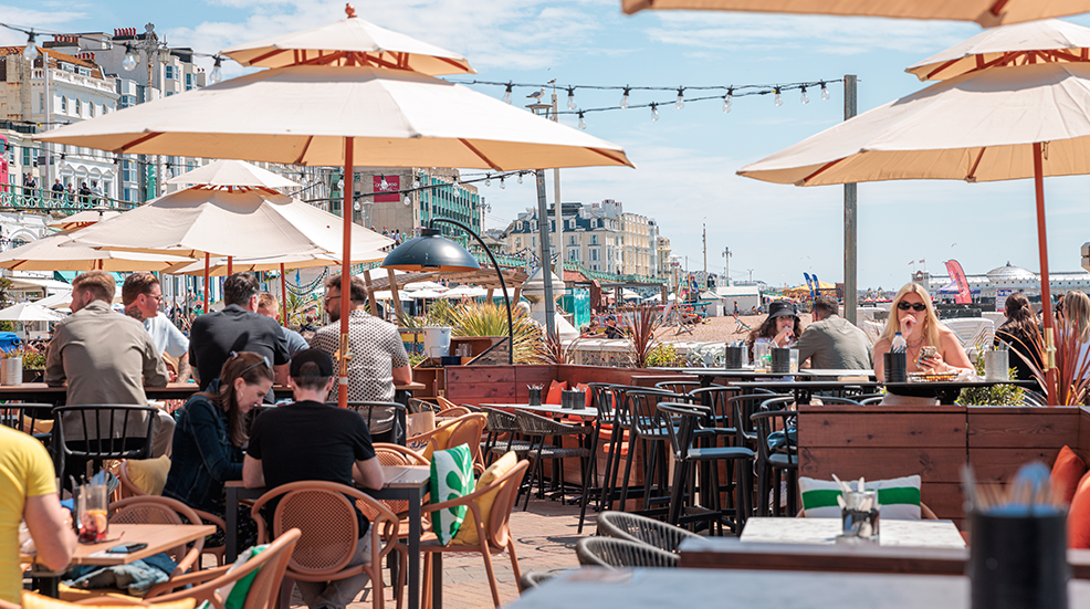 A bustling restaurant on Brighton sea front with tables, chairs, and umbrellas